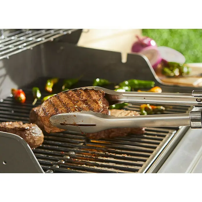 Weber Grillzange Precision - Länge: 45,72 cm - Ein saftiges Steak wird mit einer Zange auf einem Grill gewendet, umgeben von Paprika und Zwiebeln. Perfekt für ein Barbecue.