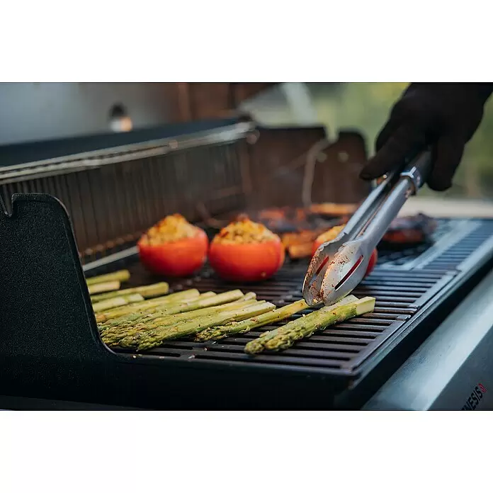Weber Crafted Parrilla para barbacoa Sear Grate - L x An: 41,4 x 40,6 cm, Hierro fundido - Una persona usa pinzas metálicas para voltear espárragos en una parrilla de gas negra. Tomates rellenos y otra comida se cocinan en la rejilla.