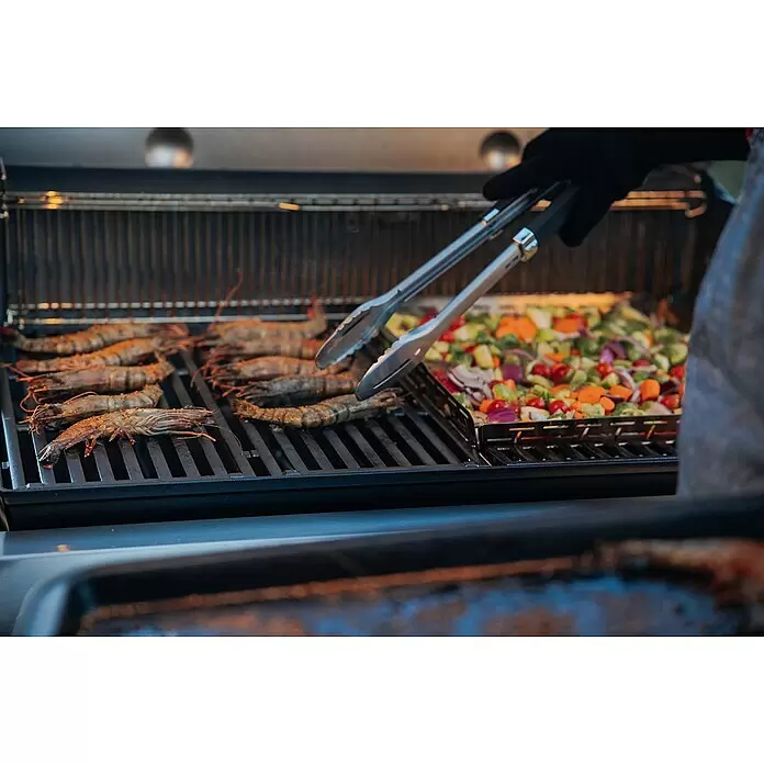 Weber Crafted Parrilla para barbacoa Sear Grate - L x An: 41,4 x 40,6 cm, Hierro fundido - Primer plano de una parrilla de gas con camarones y verduras picadas. Una persona con guante negro usa pinzas para voltear la comida.