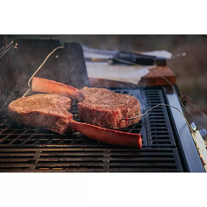 Weber Crafted Parrilla para barbacoa Sear Grate - L x An: 41,4 x 40,6 cm, Hierro fundido - Dos filetes Tomahawk sazonados cocinándose en una parrilla oscura con humo; uno tiene un termómetro de carne.