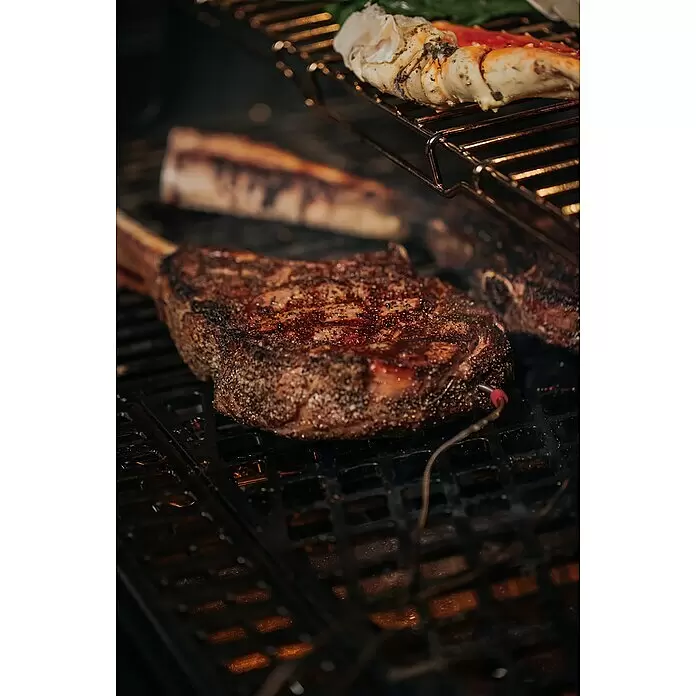 Weber Crafted Parrilla para barbacoa Sear Grate - L x An: 41,4 x 40,6 cm, Hierro fundido - Un grueso bistec sazonado con sonda de temperatura cocinándose en una parrilla caliente, con patas de cangrejo en una rejilla superior.