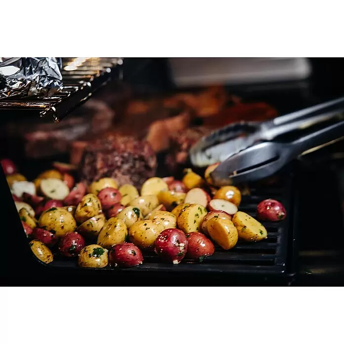 Weber Crafted Parrilla para barbacoa Sear Grate - L x An: 41,4 x 40,6 cm, Hierro fundido - Patatas rojas y amarillas sazonadas asándose con filetes borrosos al fondo.