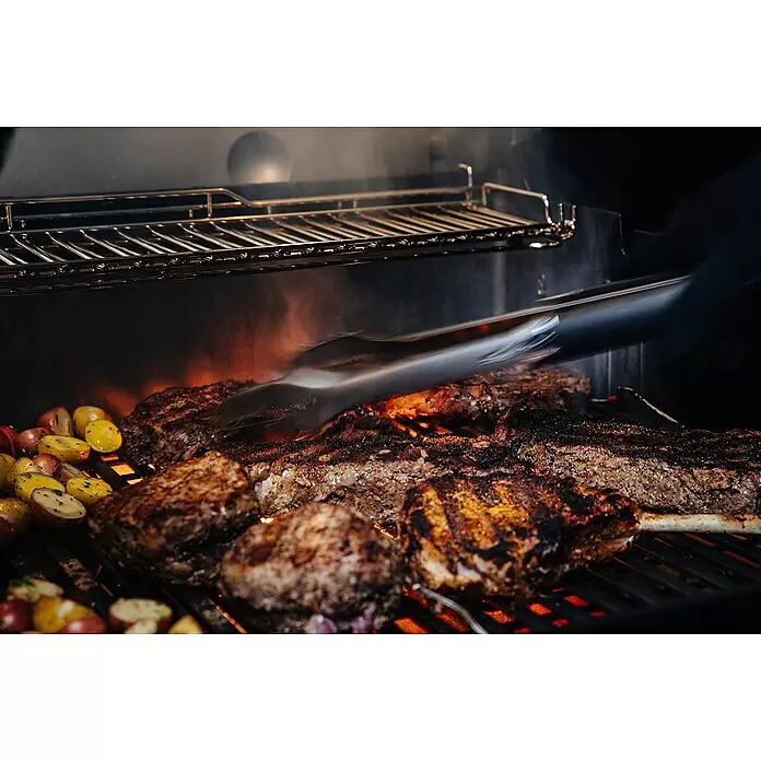 Weber Crafted Parrilla para barbacoa Sear Grate - L x An: 41,4 x 40,6 cm, Hierro fundido - Carne y patatas chispeantes en una parrilla; una persona usa tenazas para dar la vuelta a un filete entre humo y llamas.