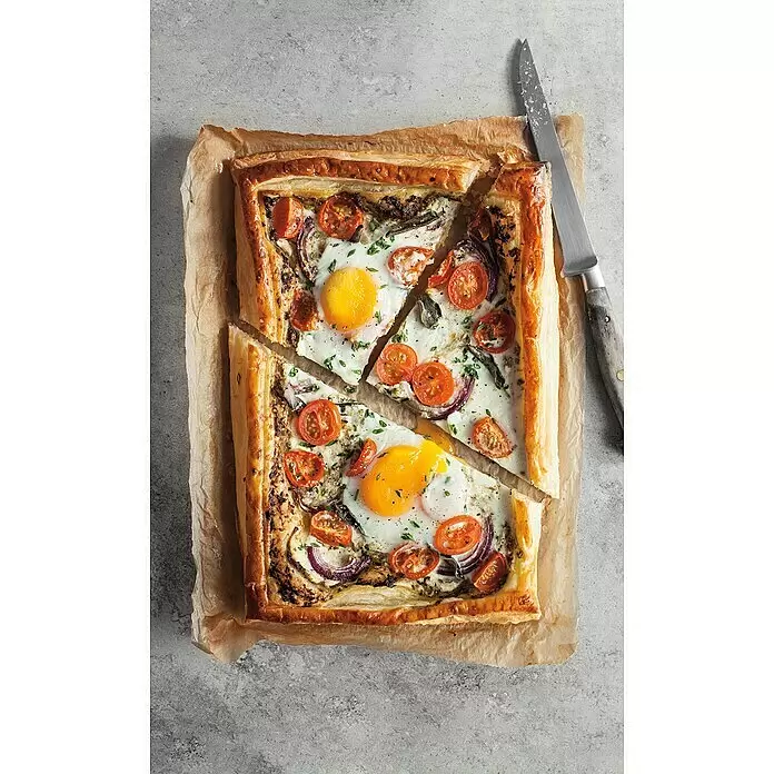 Weber Crafted Piedra para pizzas Esmaltado - L x An: 41,4 x 40,6 cm - Una tarta salada rectangular de hojaldre dorado, con dos huevos fritos, tomates cherry, cebolla morada y hierbas, cortada en trozos junto a un cuchillo.