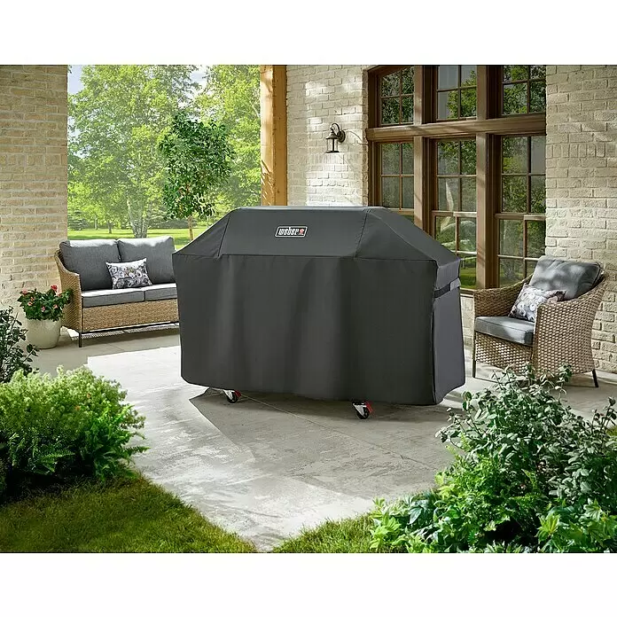 Weber Premium Grill-Schutzhülle - Passend für: Weber Genesis 400-Serie, Kunststoff - Dunkelgraue Weber Grillabdeckung auf einem Grill auf einer Terrasse, mit Gartenmöbeln und Pflanzen im Hintergrund.