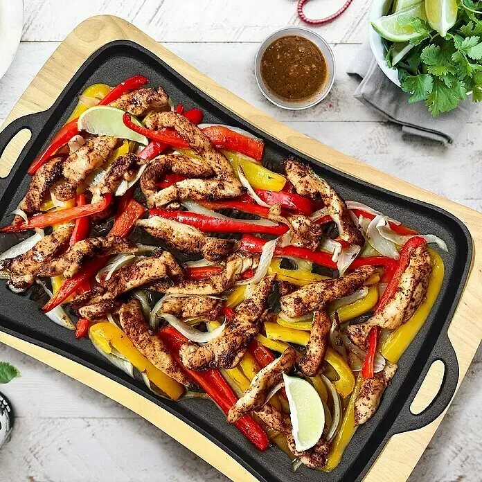 Jim Beam Grillplatte mit Holzuntersetzer - Holz, 2 -tlg. - Schwarze Gusseisen-Fajita-Servierplatte auf Holzbrett, gefüllt mit brutzelndem Hähnchen und Gemüse.