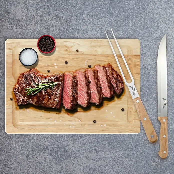 Jim Beam Schneidebrett-Set - 3 -tlg., Holz - Ein saftiges Steak, aufgeschnitten auf einem Holzbrett, mit Salz, Pfeffer und einem Jim Beam Messer und Gabel.