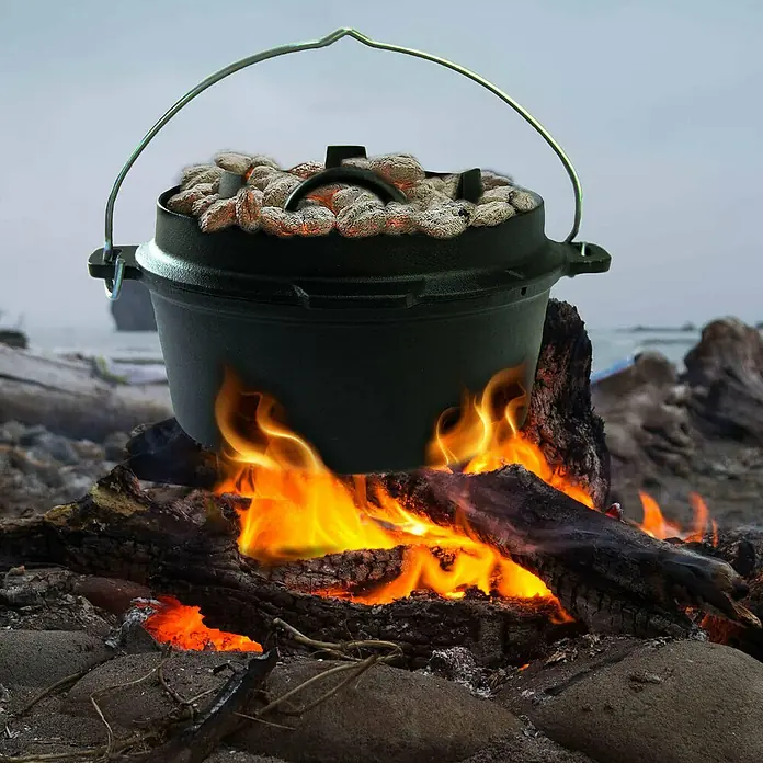 Jim Beam Dutch Oven - Ø x H: 27,2 x 19 cm - Ein gusseiserner Dutch Oven steht über einem Lagerfeuer, bedeckt mit glühenden Kohlen, perfekt zum Kochen im Freien.