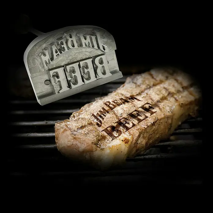Jim Beam Grillbesteck - Länge: 42 cm - Ein appetitliches Steak mit dem "Jim Beam Beef"-Branding, das mit einem glänzenden Branding-Werkzeug hervorgehoben wird.