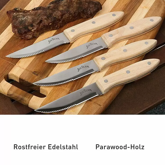 Jim Beam Steakmesser-Set - Edelstahl, Silber/Braun, 4 Stk. - Vier Jim Beam Steakmesser mit Parawood-Griff und gezackter Edelstahlklinge auf Holzschneidebrett neben Fleisch.