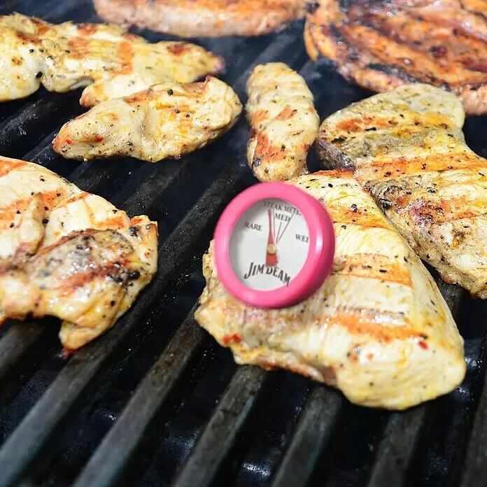 Jim Beam Grill-Thermometer - 4 Stk. - Rosafarbenes Jim Beam Fleischthermometer auf grillender Hähnchenbrust, zeigt Gargrade von RARE bis WELL.