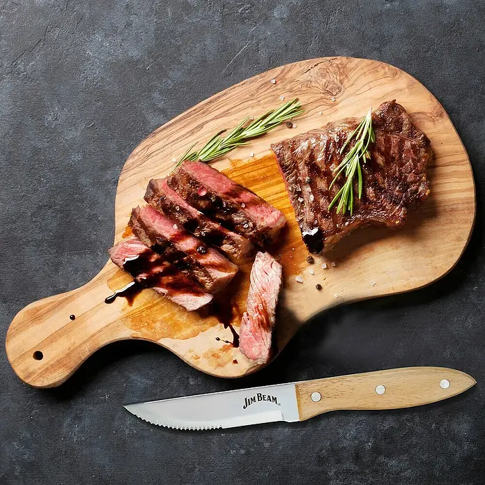 Jim Beam Steakmesser-Set - Edelstahl, Silber/Braun, 4 Stk. - Ein appetitliches Bild von einem perfekt zubereiteten Steak, serviert mit einem Jim Beam Steakmesser auf einem rustikalen Holzbrett.