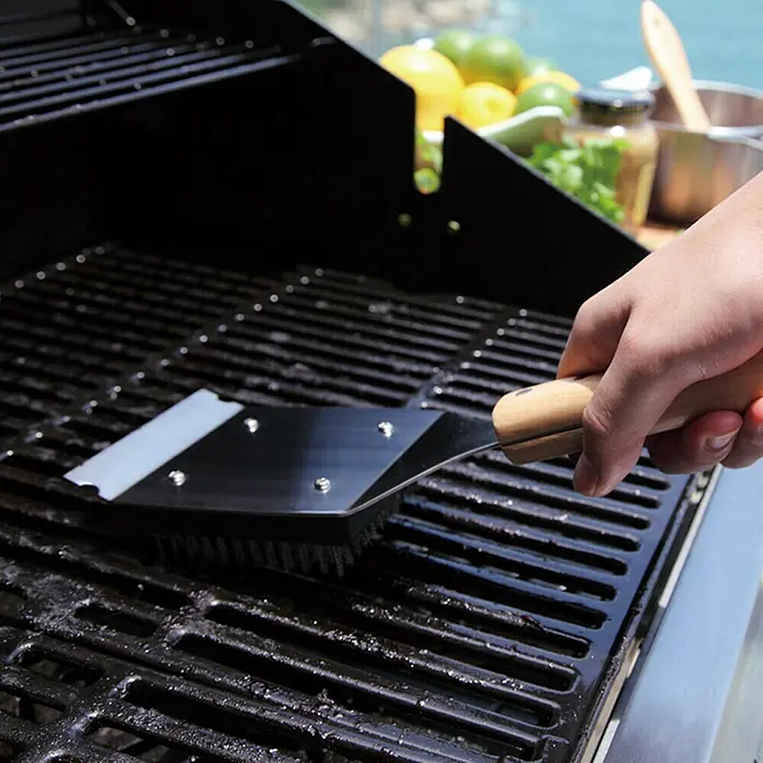 Jim Beam Grillbürste - Länge: 46 cm - Nahaufnahme einer Hand, die mit einer Grillbürste einen Grill reinigt. Die Grillbürste hat einen Holzgriff und Metallborsten.