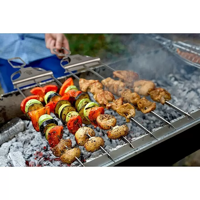 Jim Beam Grillspieß - Länge: 23,5 cm, 4 Stk. - Flache Metallspieße mit Gemüse, Pilzen und Fleisch, die über glühenden Kohlen gegrillt werden, von einer Hand gehalten.