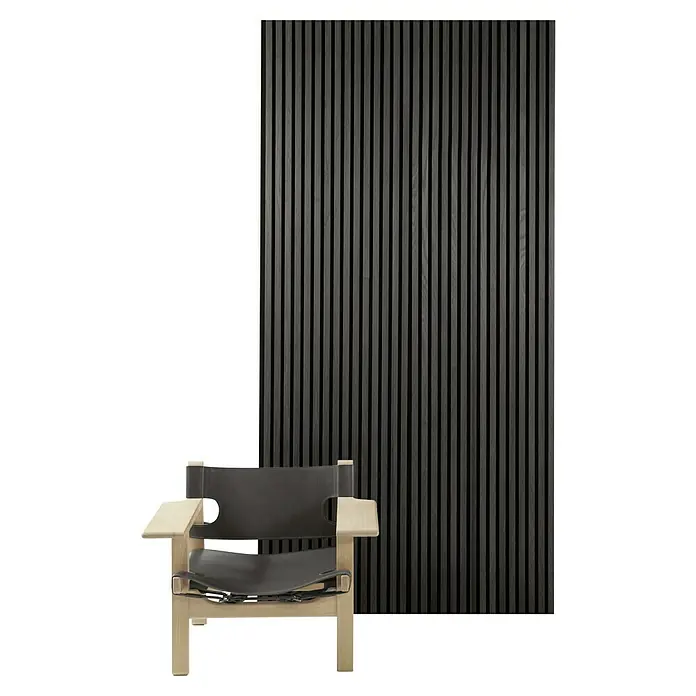 FibroTech Akustikpaneel Premium - Black Oak, 2.440 x 605 x 22 mm - Schwarzer Holzlattenwandpaneel und ein stilvoller Sessel mit hellem Holzrahmen und dunklen Lederdetails schaffen ein modernes Ambiente.