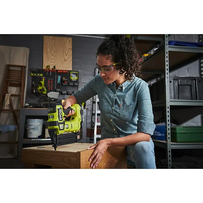 Ryobi ONE+ Maschinenpaket - Akku-Nagler R18GN18X-0 + gratis Starter-Kit - Frau arbeitet mit einem RYOBI Nagler an einem Holzprojekt, Schutzbrille trägt. Das Gerät ist Akku-betrieben und benutzerfreundlich.