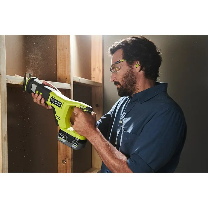 Ryobi ONE+ Akku-Säbelsäge RRS18-0 - 18 V - Mann benutzt eine gelbe Ryobi-Säbelsäge zum Schneiden von Holz, wobei er Schutzbrille und Ohrstöpsel trägt.