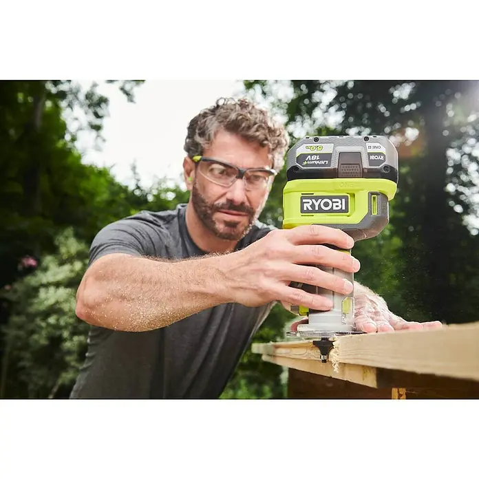 Ryobi ONE+ Akku-Kantenfräser RTR18-0 - 18 V, Ohne Akku, Leerlaufdrehzahl: 20.000 U/min - 30.000 U/min - Ein Mann verwendet eine Ryobi Oberfräse, um ein Holzbrett zu bearbeiten. Die Fräse ist gelb und schwarz mit einem Akku oben.