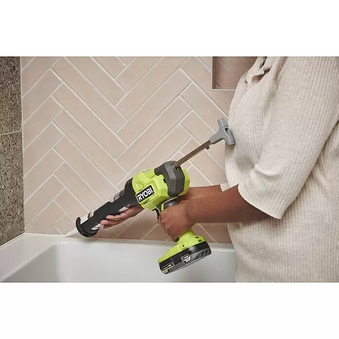 Ryobi ONE+ Maschinen-Set - Akku-Kartuschenpresse RCG18-0 + gratis Starter-Kit - Kalkgrüne Ryobi Kartuschenpistole beim Auftragen von weißem Dichtstoff an Wanne und Fliesen.