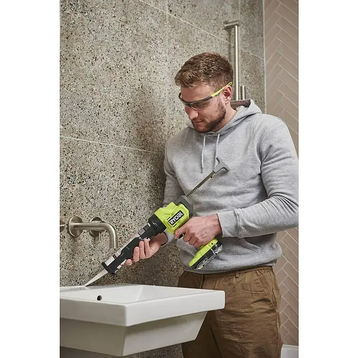 Ryobi ONE+ Maschinenpaket - Akku-Kartuschenpresse RCG18-0 + gratis Starter-Kit - Ein Mann benutzt eine Ryobi-Dichtpistole, um eine Spüle abzudichten. Die Akku-Dichtpistole sorgt für gleichmäßiges Auftragen.