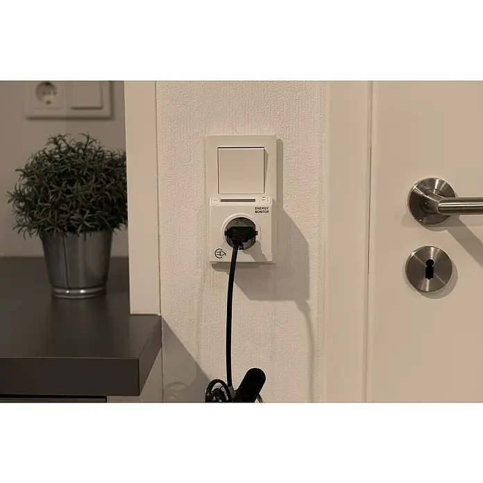 REV Energiekosten-Messgerät - Leistung: 3.680 W - Ein Energiekosten-Messgerät ist an der Wand montiert und misst den Stromverbrauch. Das Gerät ist weiß und hat eine digitale Anzeige.