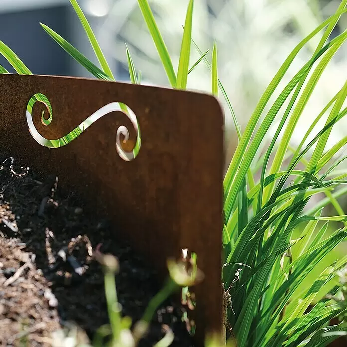 Bellissa Kräuterspirale Corten - 130 x 140 x 80 cm - Rostige Metall-Gartenbegrenzung mit Schnörkelmuster, mit Erde und grünem Gras gefüllt.
