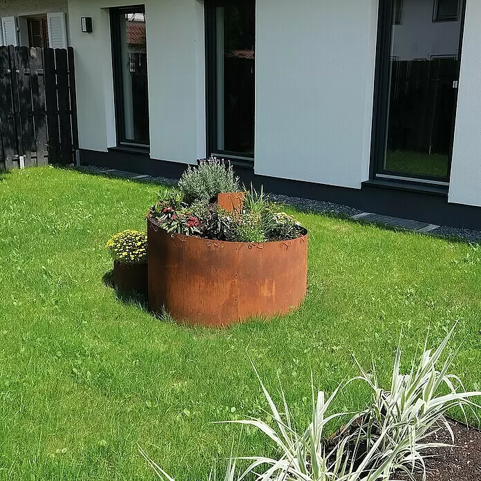 Bellissa Kräuterspirale Corten - 130 x 140 x 80 cm - Ein großer, runder Rostmetall-Pflanzkübel, mit bunten Blumen in einem grünen Garten.