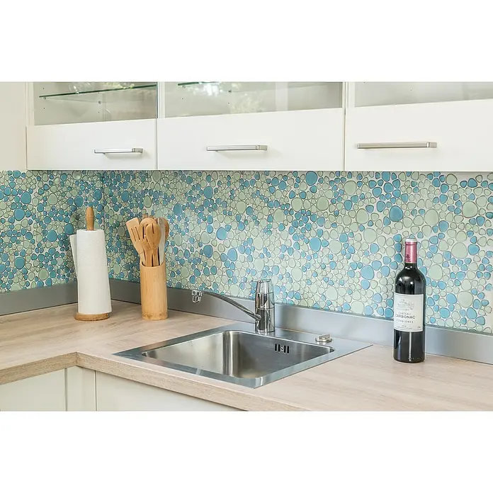 Mosaikfliese Kiesel XKM 79 - 30 x 30 cm, Hellblau/Hellgrün, Glänzend - Küchendekor mit einer Flasche Rotwein, einem Spülbecken und farbenfrohen Fliesen, die der Szene einen Hauch von Raffinesse verleihen.