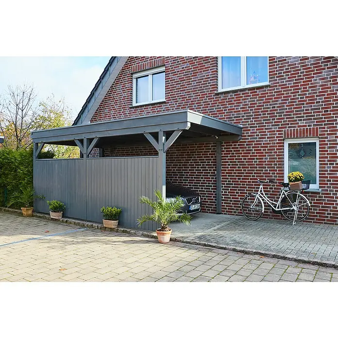 swingcolor Holzlasur - Silberholz, 2,5 l, Seidenglänzend - Das Bild zeigt ein Carport aus Holz mit einem grauen Anstrich, angebaut an ein Backsteingebäude, mit einem Auto darin und einem Fahrrad davor.