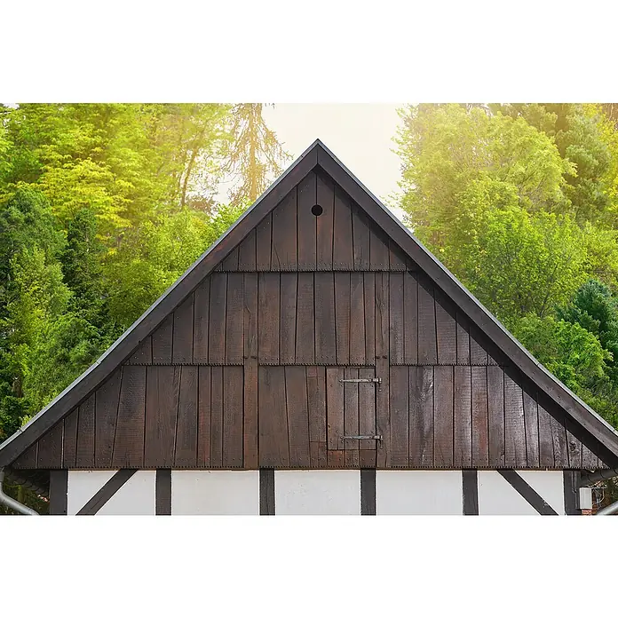 swingcolor Premium Holzlasur - Kastanie, 750 ml, Seidenglänzend - Detailaufnahme des hölzernen Giebels eines traditionellen Hauses, umgeben von üppigem Grün und strahlendem Sonnenlicht.