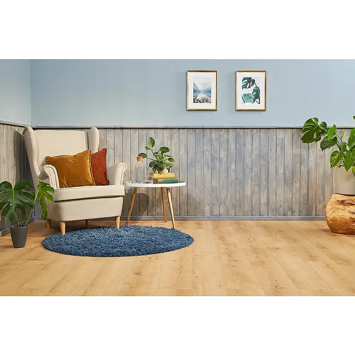 swingcolor Holzlasur Innenlasur - Nebelgrau, 750 ml, Seidenmatt - Einladende Leseecke mit beigem Sessel, blauer Teppich, Holzboden und Wandpaneelen. Zwei goldgerahmte Bilder schmücken die hellblaue Wand.