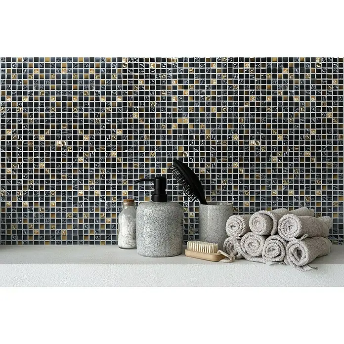 Mosaikfliese Crystal Mix XCM M650 - 30 x 30 cm, Schwarz/Gold, Glänzend - Badezimmer-Arrangement mit Handtüchern, Seifenspender, Bürste und Dekoration vor einer Mosaikwand.
