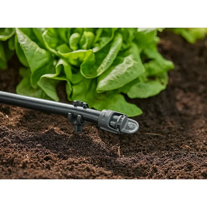Gardena Micro-Drip Tapón de sellado - 4 ud., ½″ - Primer plano de un sistema de riego con manguera negra y emisor gris, ubicado en la tierra junto a plantas de lechuga.