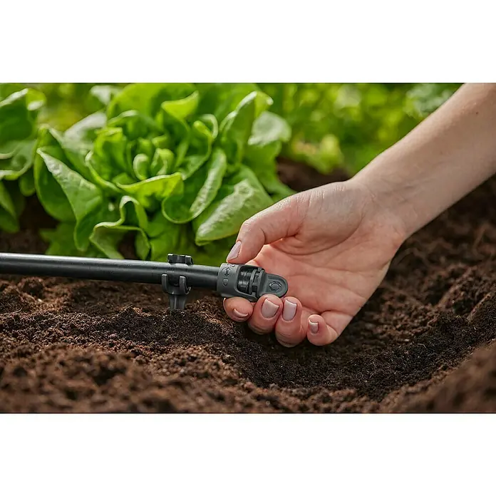 Gardena Micro-Drip Tapón de sellado - 4 ud., ½″ - Primer plano de una mano ajustando un sistema de riego por goteo en un jardín, con lechugas al fondo.