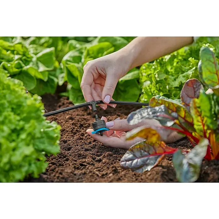 Gardena Micro-Drip Pieza T - ³⁄₁₆'', 10 ud. - Primer plano de una persona instalando un sistema de riego para plantas en un jardín, permitiendo una entrega de agua eficiente.