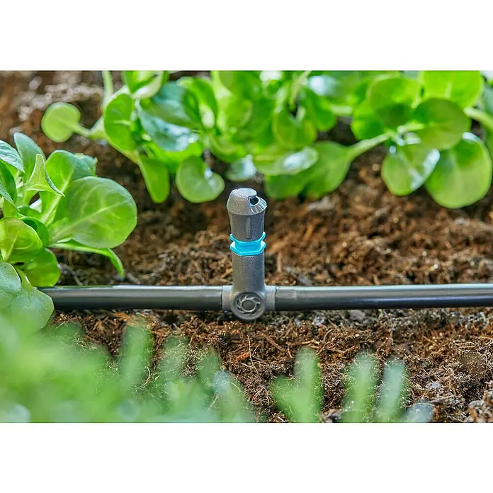 Gardena Micro-Drip Pieza T - ³⁄₁₆'', 10 ud. - Primer plano de un aspersor de un sistema de riego con una línea negra en medio de una vegetación exuberante.