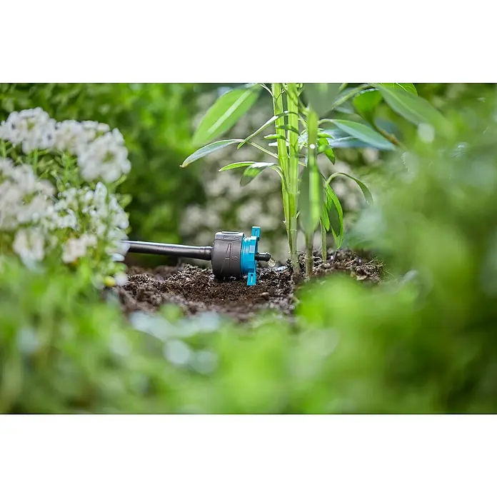 Gardena Micro-Drip Gotero final regulable - 6 ud., 8 l/h - Primer plano de un sistema de riego con un regulador ajustable que dispensa agua a plantas jóvenes, entre exuberante vegetación.