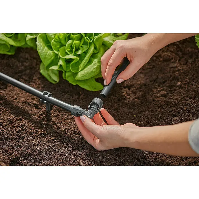 Gardena Micro-Drip Codo - Diámetro: 13 mm - Imagen de una persona conectando un sistema de riego con un codo y un trozo de tubo mientras la lechuga crece al fondo.