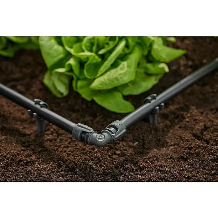 Gardena Micro-Drip Codo - Diámetro: 13 mm - Primer plano de un sistema de riego por goteo con tubos y conectores, dispuesto en el suelo junto a plantas de lechuga.