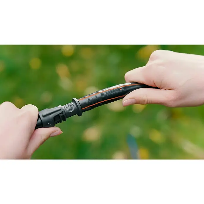Gardena Tubo distribuidor Flex - 50 m, ½″ - Primer plano de manos manipulando un accesorio de herramienta de jardín negro con detalles naranja y un mecanismo giratorio.