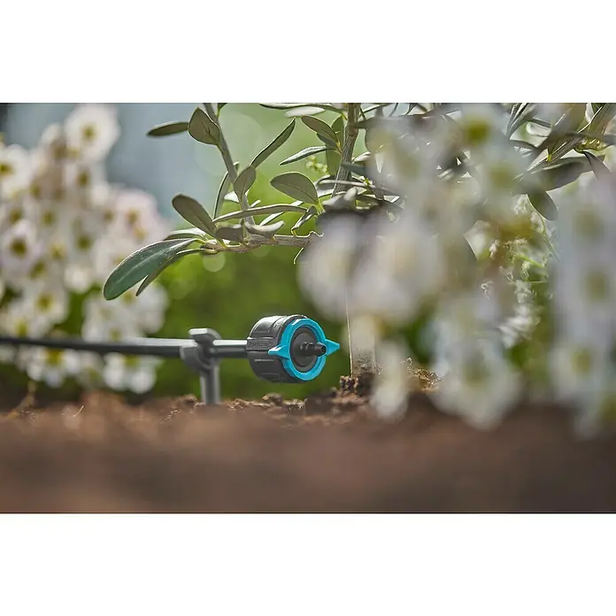 Gardena Micro-Drip Gotero final regulable - 6 ud., 8 l/h - Primer plano de un sistema de microgoteo GARDENA para el riego de plantas, enclavado en la tierra, con flora al fondo.