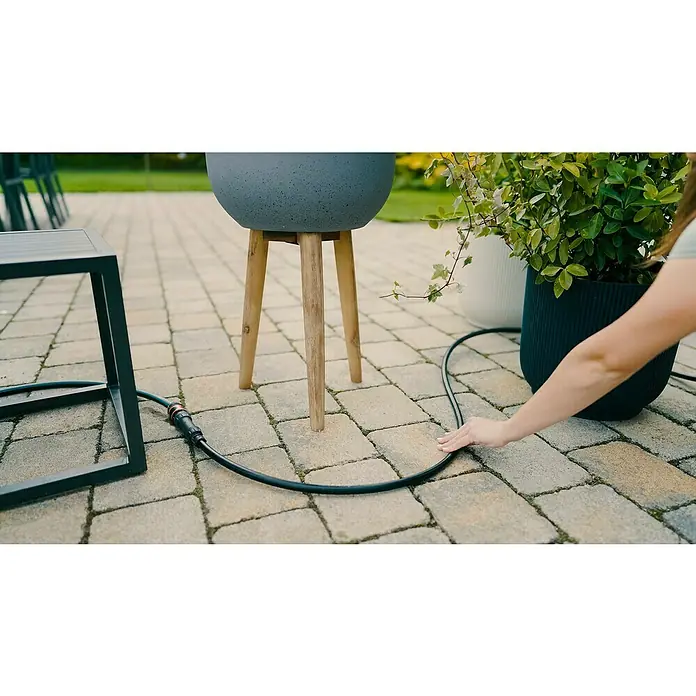 Gardena Tubo distribuidor Flex - 50 m, ½″ - Primer plano de una mujer instalando una manguera de riego negra para plantas en el jardín para proporcionar riego automático.