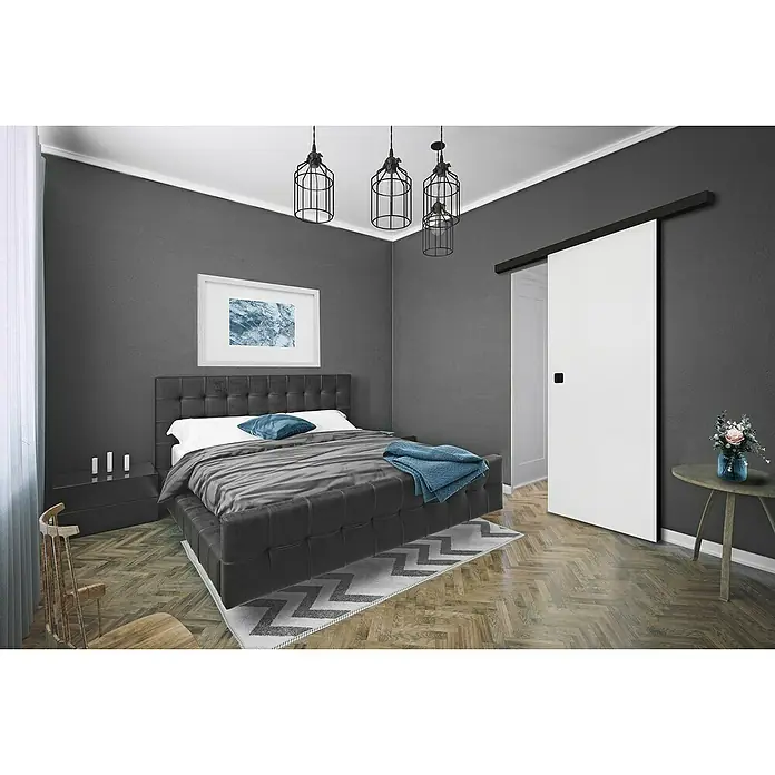 Diamond Doors Black Edition Holzschiebetür Edge - 935 x 2.058 mm, Verkehrsweiß matt, Schwarz, Material Mittellage: Wabe - Ein Schlafzimmer mit einem dunklen Bett mit gestepptem Kopfteil, schwarzen Nachttischen und einer Schiebetür neben einem runden Beistelltisch.