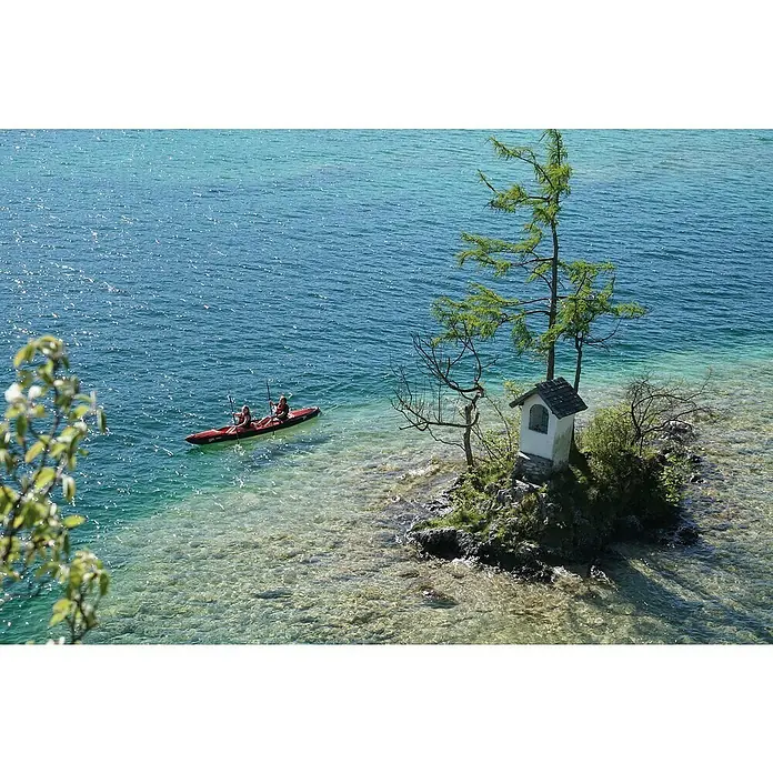 Grabner Kajak Mega - L x B: 500 x 90 cm, Geeignet für: 2 Personen, Nutzlast: 280 kg - Ein rotes Kajak mit zwei Personen gleitet auf dem kristallklaren Wasser, in der Nähe einer kleinen Insel mit einem Miniaturhaus.