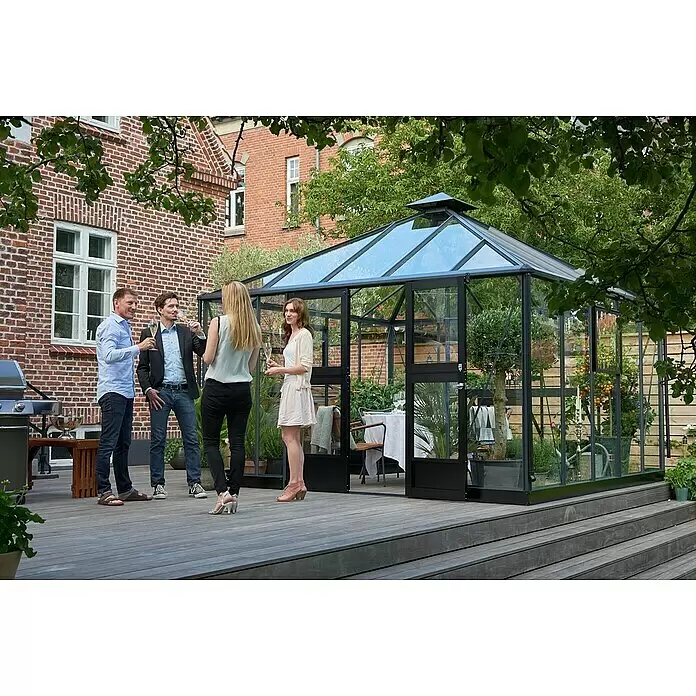 Juliana Gewächshaus Oase - Außenmaß inkl. Dachüberstand (B x T): 368 x 368 cm, Material Seitenwand: Glas, 3 mm, Anthrazit/Schwarz - Schwarz gerahmtes Glasgewächshaus auf Holzterrasse mit geselligen Menschen. Innen sind Esstisch und Pflanzen sichtbar.