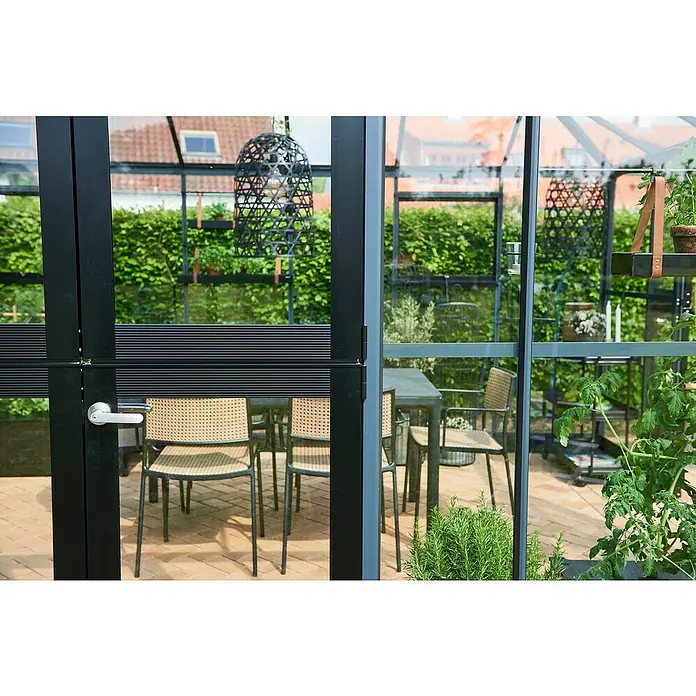 Juliana Gewächshaus Grand Oase - Außenmaß inkl. Dachüberstand (B x T): 296 x 439 cm, Material Seitenwand: Glas, 3 mm, Anthrazit/Schwarz - Einladende Gartenszene durch eine Glasveranda mit schwarzen Rahmen und einladenden Korbstühlen.