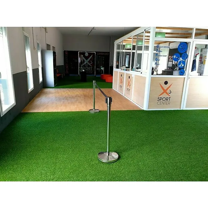 Césped artificial Bahia - 5 x 2 m, Altura del pelo: 18 mm, 26.250 puntadas/m² - Vista de un gimnasio con césped artificial y postes de barrera que guían el camino. También se muestra una zona de recepción en la imagen.