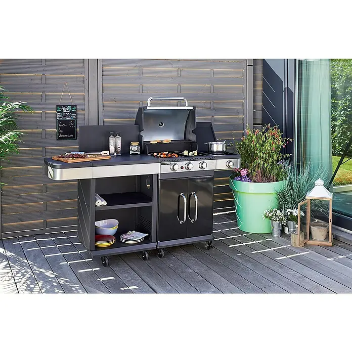 Barbacoa de gas Fidgi - Superficie de la parrilla (An x Pr): 57,5 x 42 cm, 11,5 kW, Número de quemadores: 3 - Una parrilla negra moderna con detalles de acero inoxidable en un patio, rodeada de plantas y decoración, perfecta para barbacoas de verano.