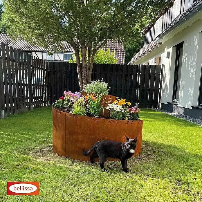 Bellissa Kräuterspirale Corten - 130 x 140 x 80 cm - Rostfarbenes Hochbeet aus Metall mit Blumen, um einen Baum herum in einem Garten.
