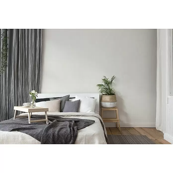 A.S. Création Trendwall 2 Vliestapete - Reinweiß, Uni, 10,05 x 0,53 m - Ein Schlafzimmer mit weißem Bett, grauen Kissen und einer dunkelgrauen Decke. Ein Holz-Frühstückstablett mit Blumen steht auf dem Bett.